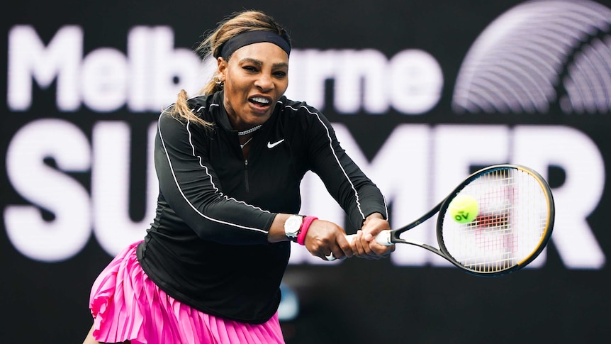 Serena Williams plays a two-handed backhand wearing a black long-sleeved top and pink skirt