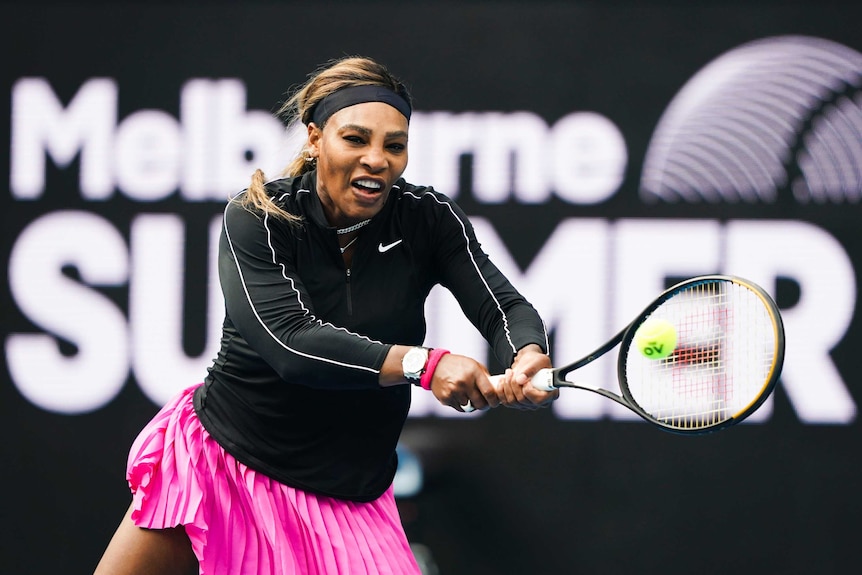 Serena Williams plays a two-handed backhand wearing a black long-sleeved top and pink skirt