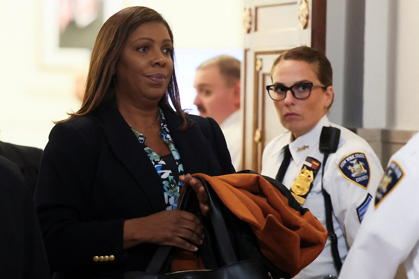Letitia James holds a jacket as she  walks out of a court room next to a female security guard.
