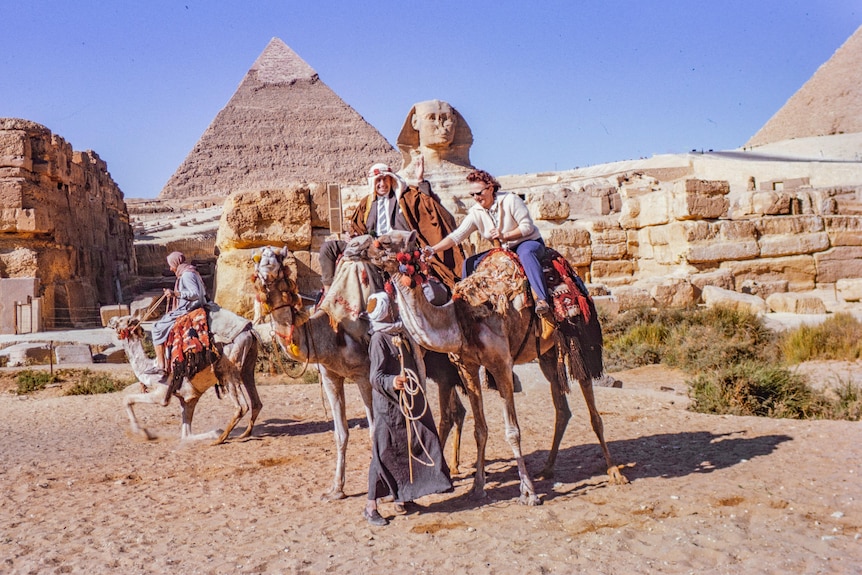 Two people riding camels in front of the sphinx in Egypt.