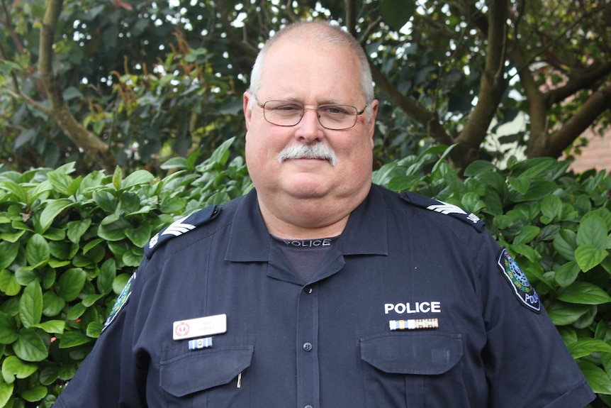 Sergeant Andy Stott standing in front of greenery. He is wearing his police uniform.