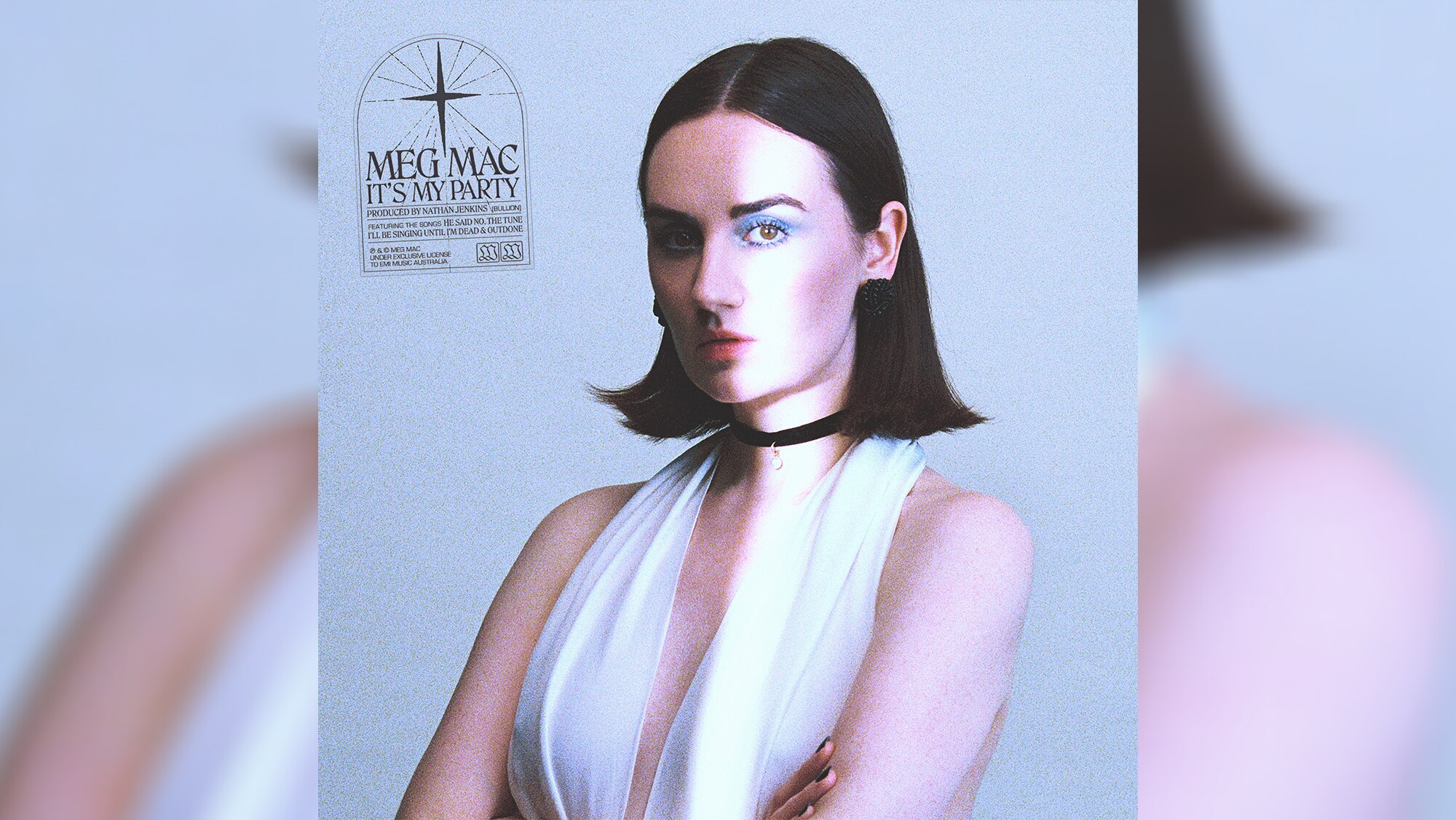 Portrait of woman with black hair wearing white top and choker, arms crossed against pale blue backdrop. 