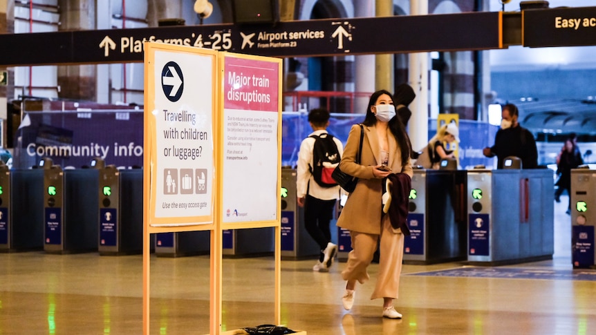A woman in a face mask walks in front of train station turnstiles.