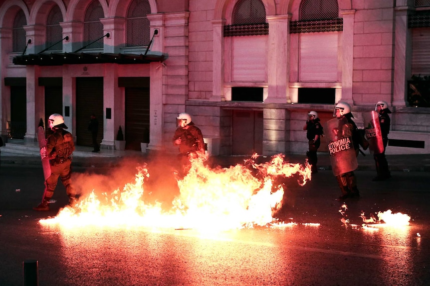 Small fires surround riot police on a street in Athens.