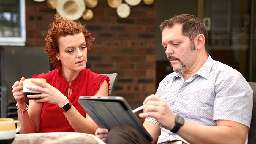 A woman and a man sitting and going over their energy bills, with an iPad and cups of coffee