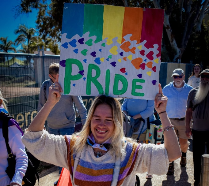 A woman holding a sign with the word Pride and rainbow hearts.