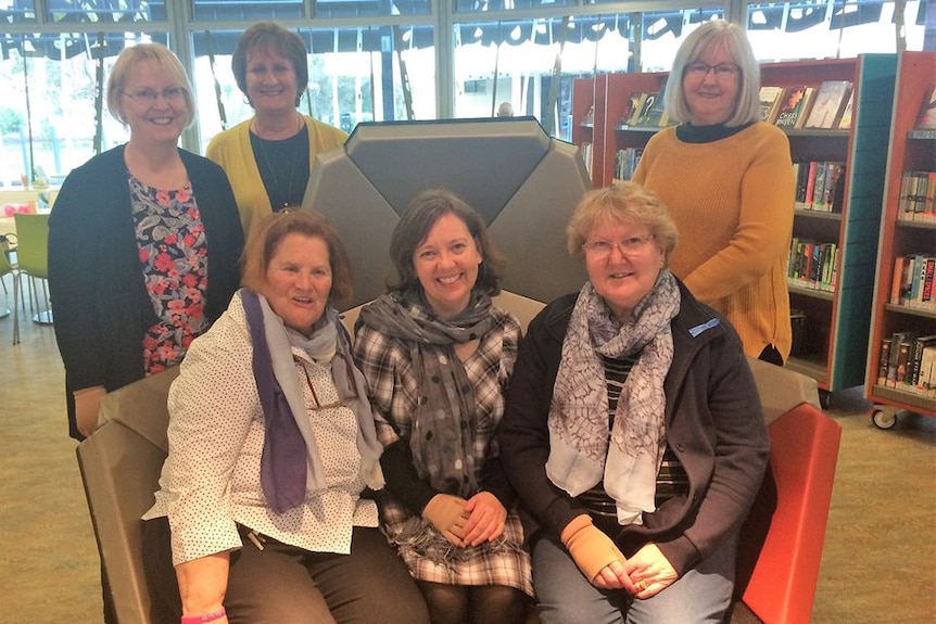 A group of six smiling women together in a library