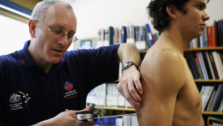 An AFL staff member pinches the back of a player's arm with a skin fold test instrument