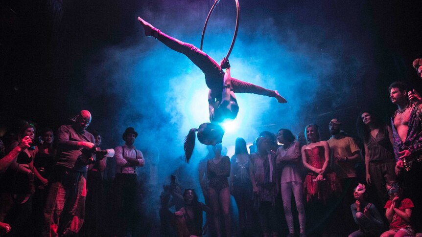 An acrobat handing from a ring with purple lighting