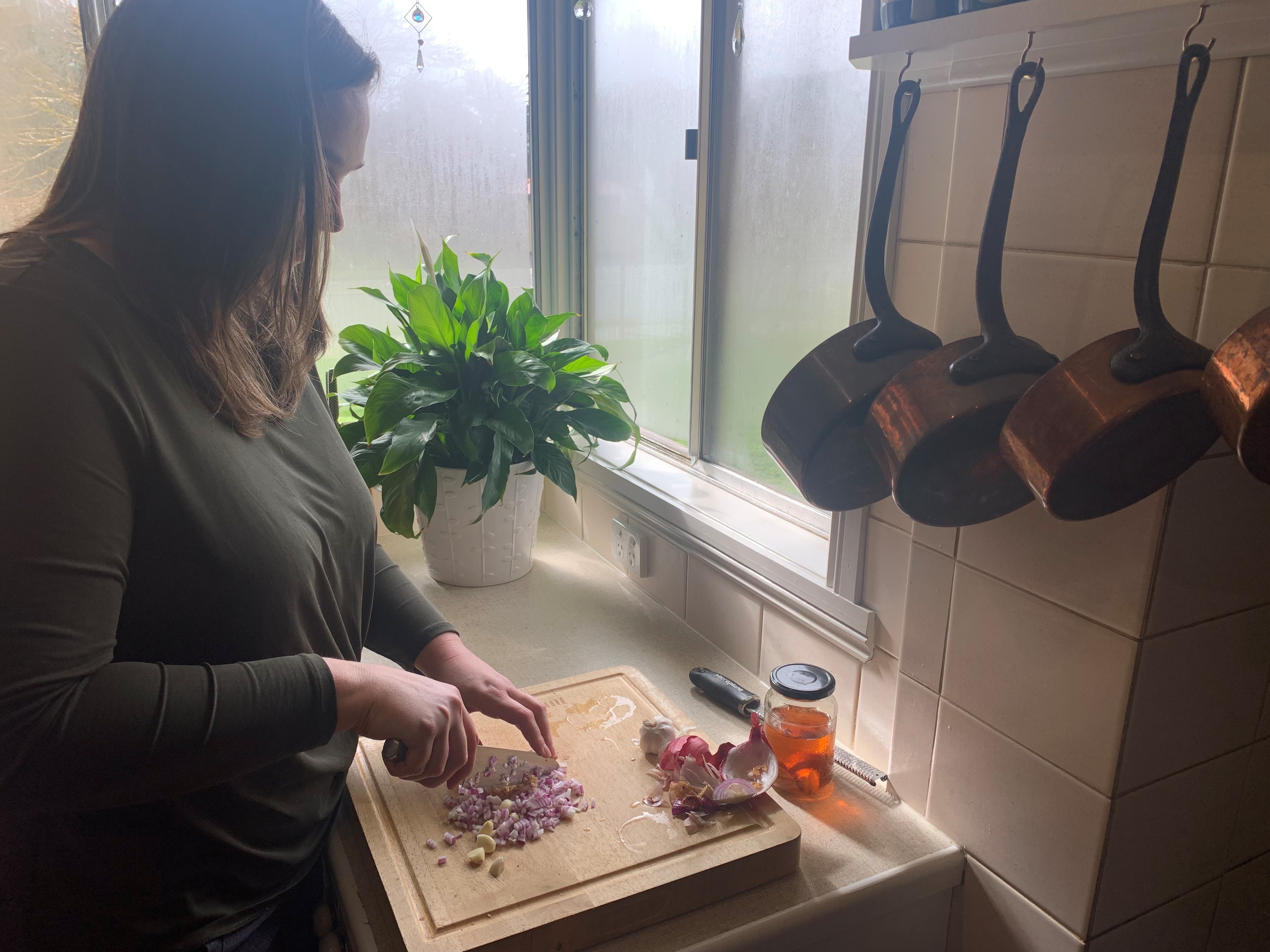 Anna Deacon chopping ginger, onions and garlic with a knife on a wooden board.