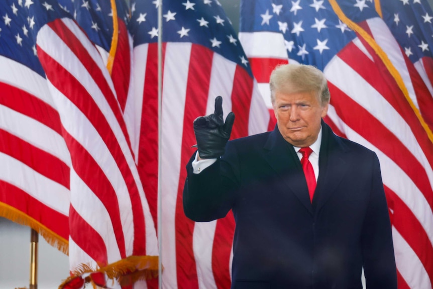 US President Donald Trump stands in front of American flags.