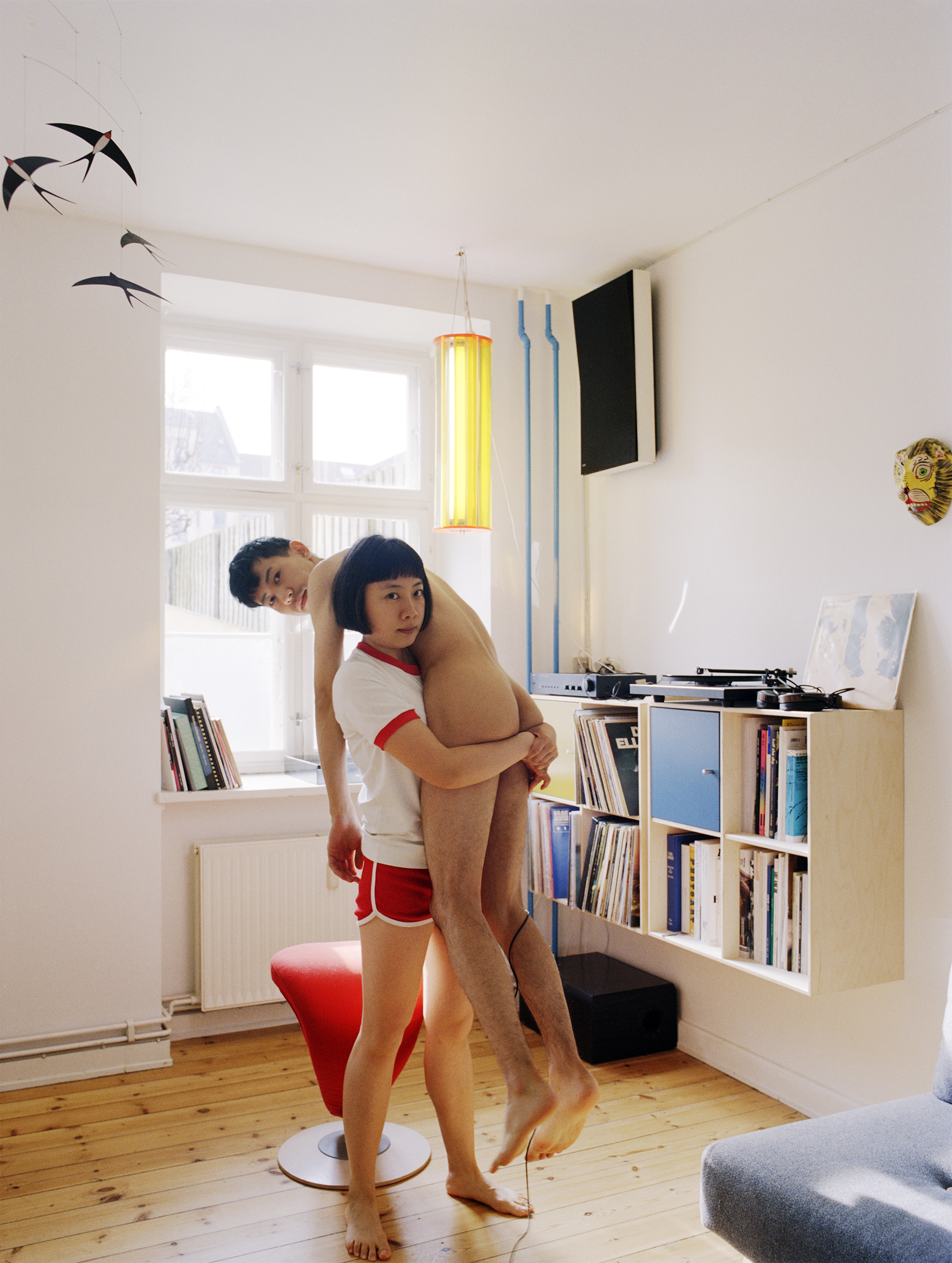 Pixy Liao, a 30-something Chinese woman with a short bob wears red and white sports clothes and carries a naked Japanese man.