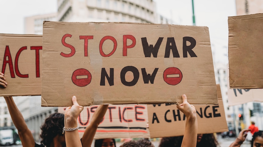 A protester holds a cardboard signs that reads "No War"