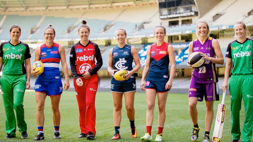 Photo shoot of female athletes from various Australian sports codes lined up on a field in a stadium.