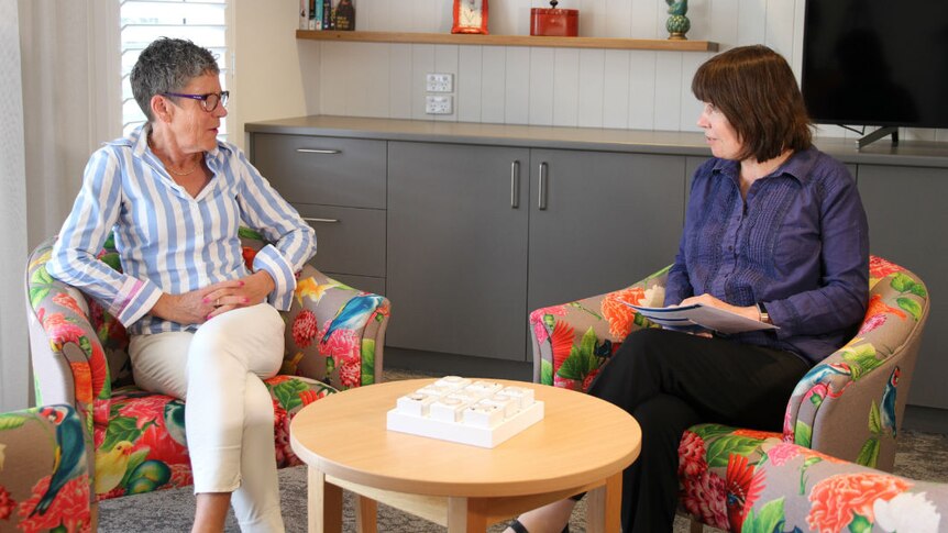 A woman with short grey hair and a woman with medium-length grey hair sitting in armchairs talking.