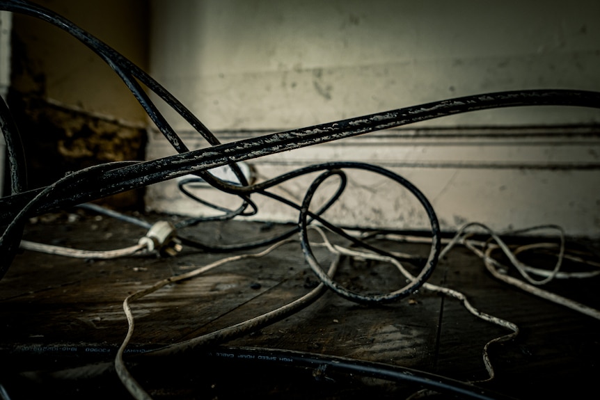 Frayed wires coated in mud are in a pile on the floor of a flood-damaged house