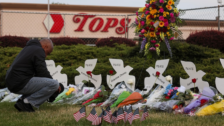 A man kneels in front of memorials to the victims of the shooting.