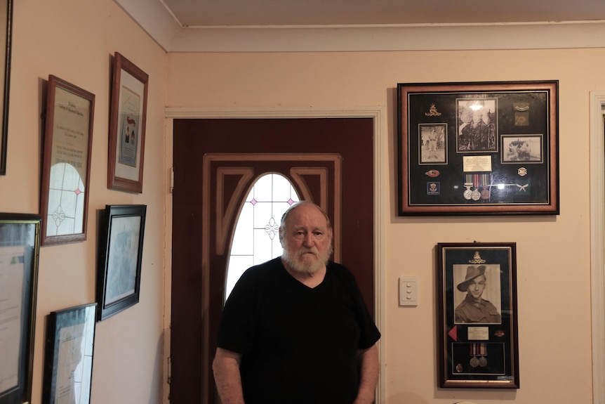 Jon Eaton stands in front of door with framed accolades on the walls either side of him. 