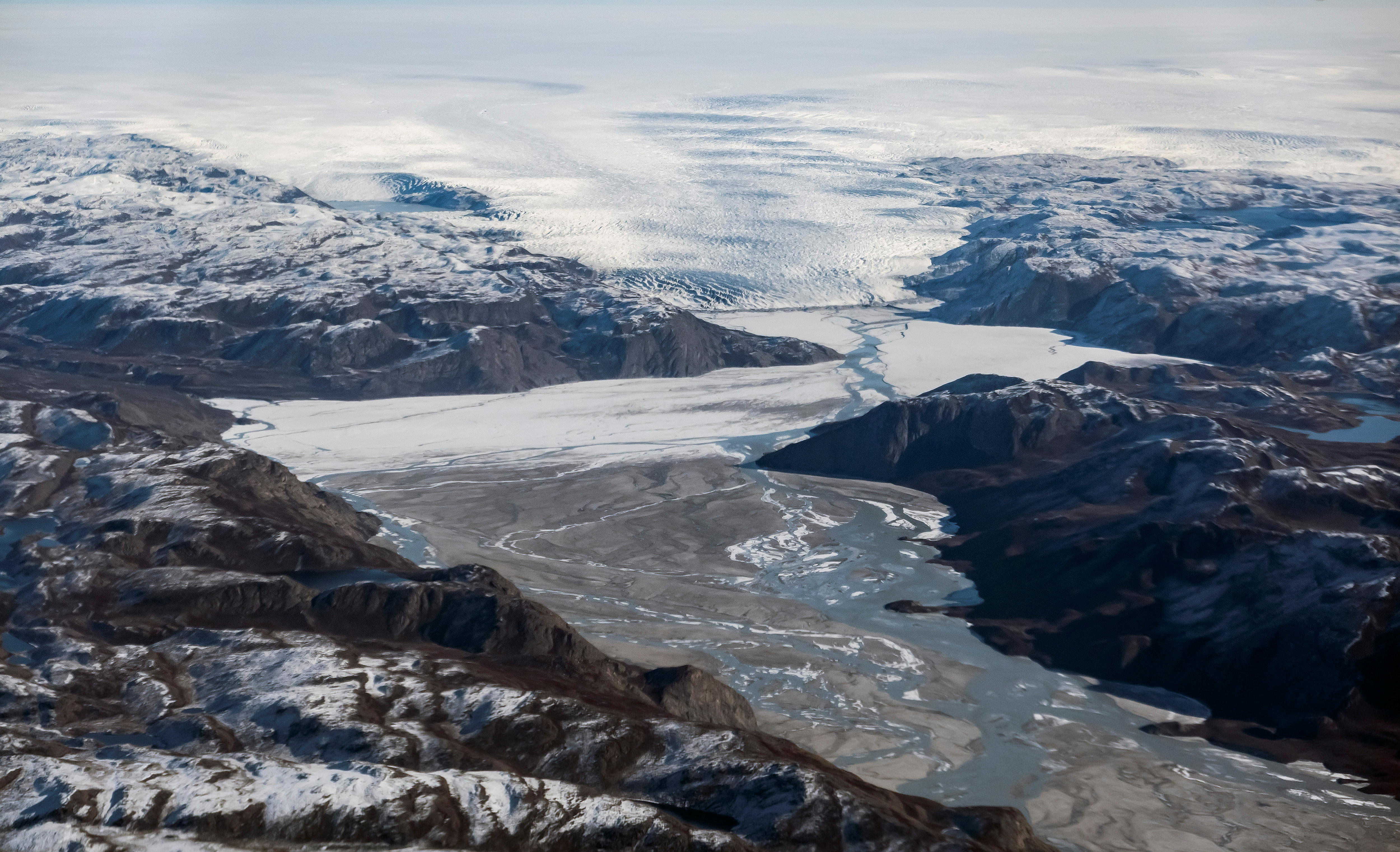 A glacier mixed with water and ice runs through snow covered mountains