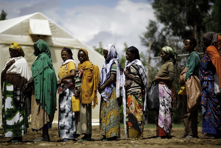 A group of Ethiopian women line up to collect food wearing colourful skirts and head wraps.