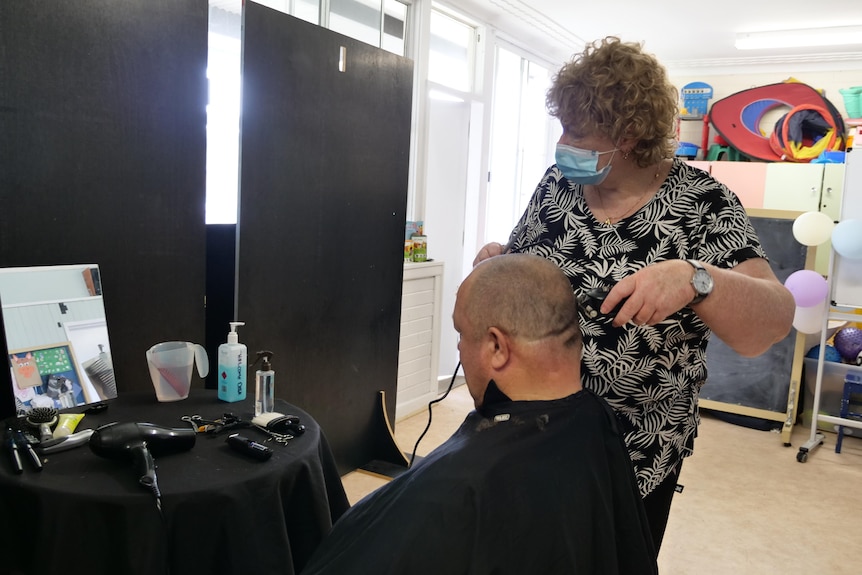 A woman gives a man a haircut.