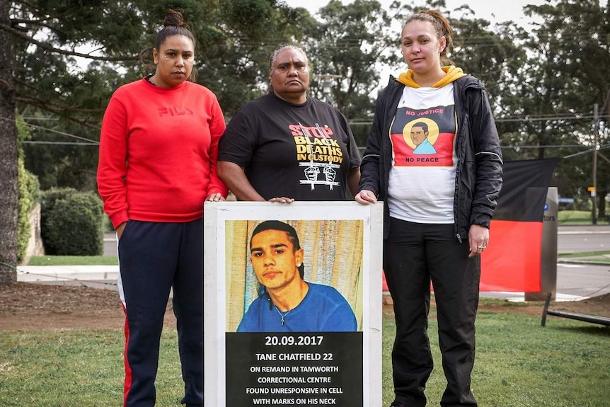 Three Indigenous women hold a portrait of Tane Chatfield