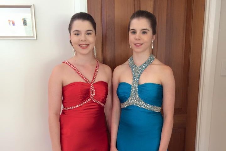 Two girls in formal dresses stand next to each other.