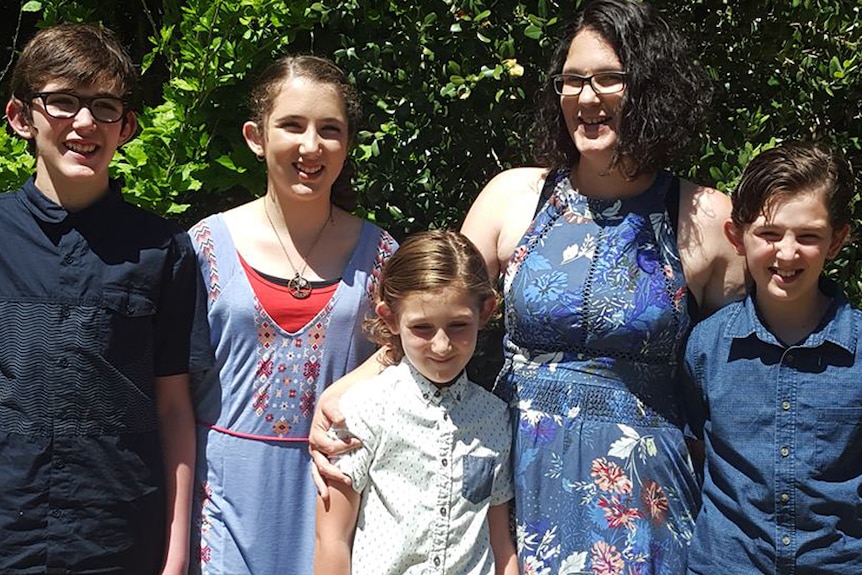 Katrina Miles stands with trees in the background with her four children.