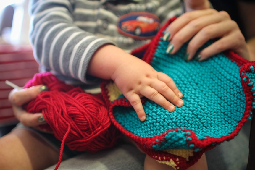 A young mother and her son hold a blanket square knitted for the victims of family violence.