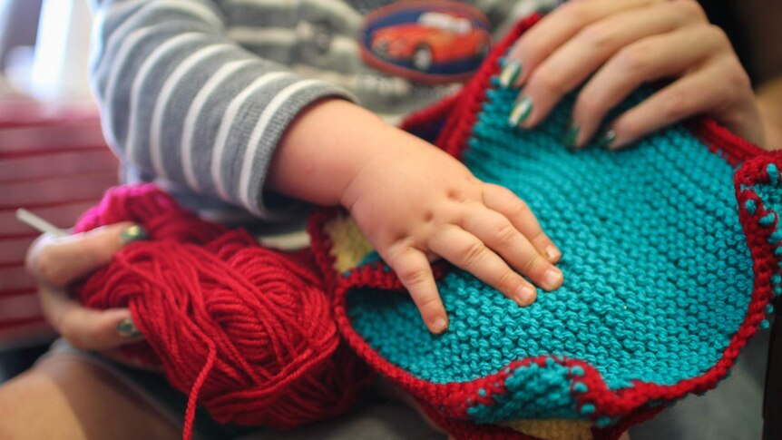 A young mother and her son hold a blanket square knitted for the victims of family violence.