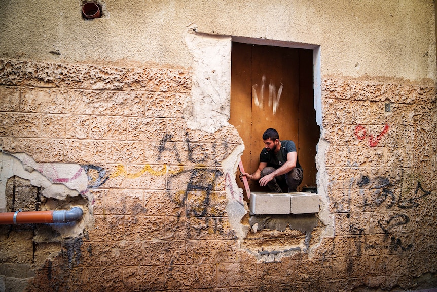 A man works on a hole in a destroyed brick wall in Jenin