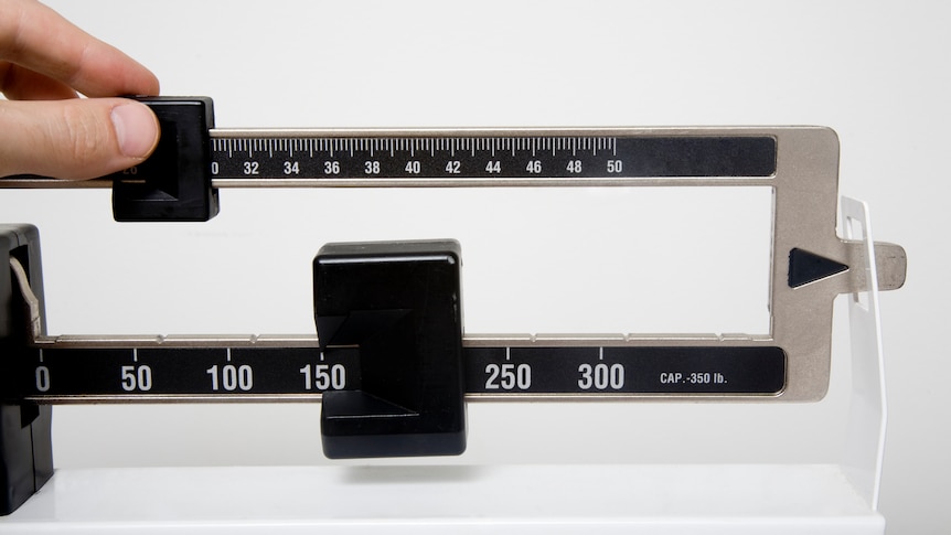 A stand up doctor's office style scale with a hand calculating the weight