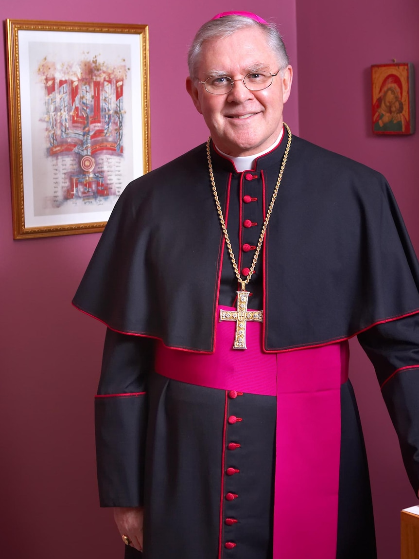 Archbishop Mark Coleridge in robes smiling at camera in a room with purple paint.