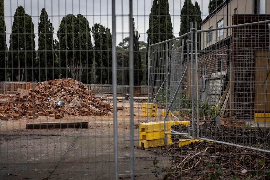 A pile of bricks sits behind a construction fence, next to a townhouse still standing.