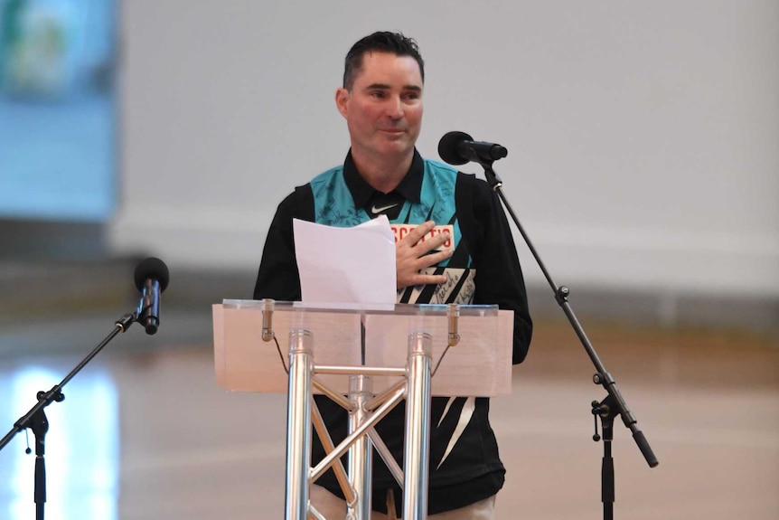 Luke Naismith standing at a lectern speaking into a microphone