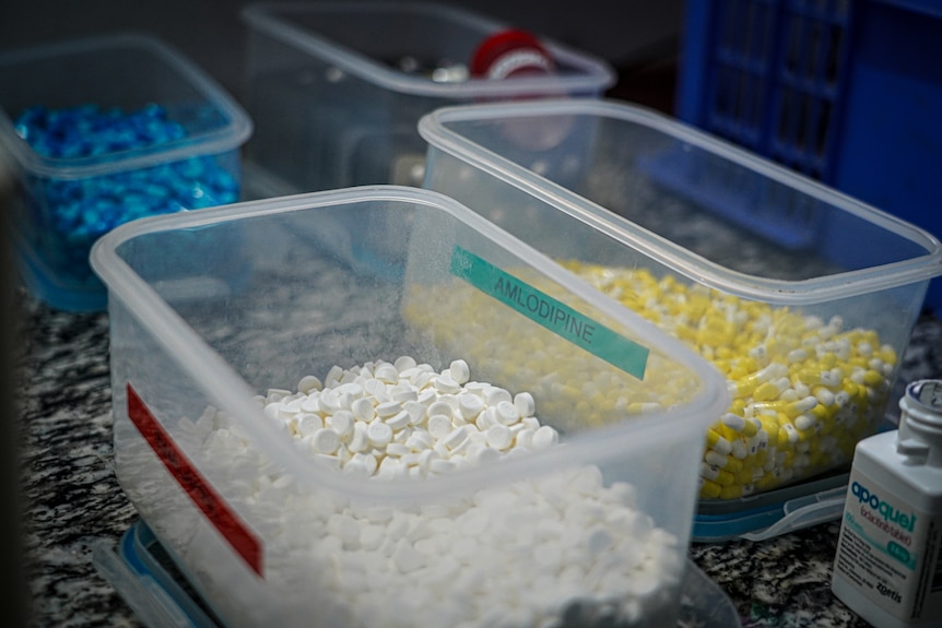 Two large plastic containers, one with white pills and another with yellow and white capsules.