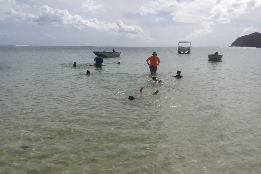 Children swimming with an instructor in an island lagoon.