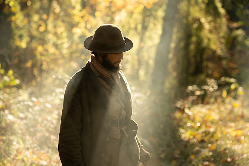 Film still of John Magaro as Cookie standing in the woods in First Cow