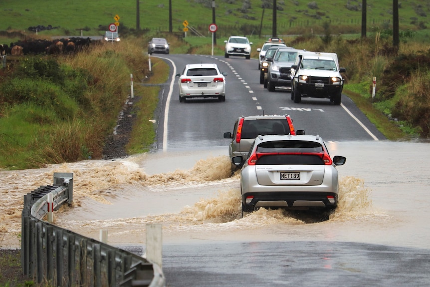 Two cars driving through a flooded road. 
