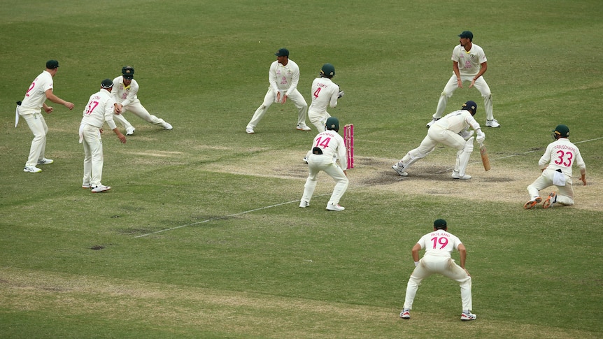 A crowd of fielders surround the batter, who watches on as David Warner catches the ball