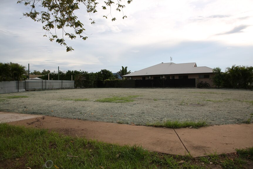 An empty residential lot in a Palmerston suburb, with some trees and greenery visible.