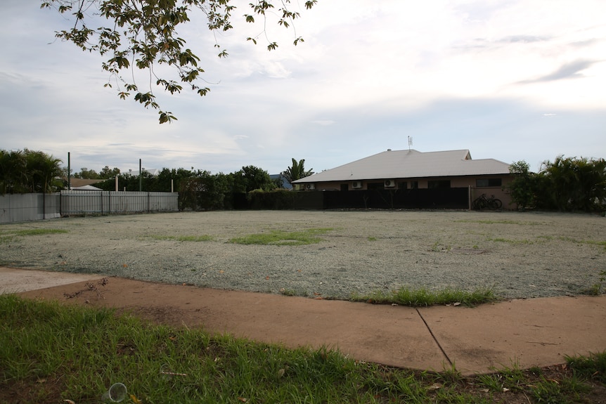 An empty residential lot in a Palmerston suburb, with some trees and greenery visible.