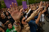 A large crowd of people - mainly women - hold their hands in the air with their fingers extended