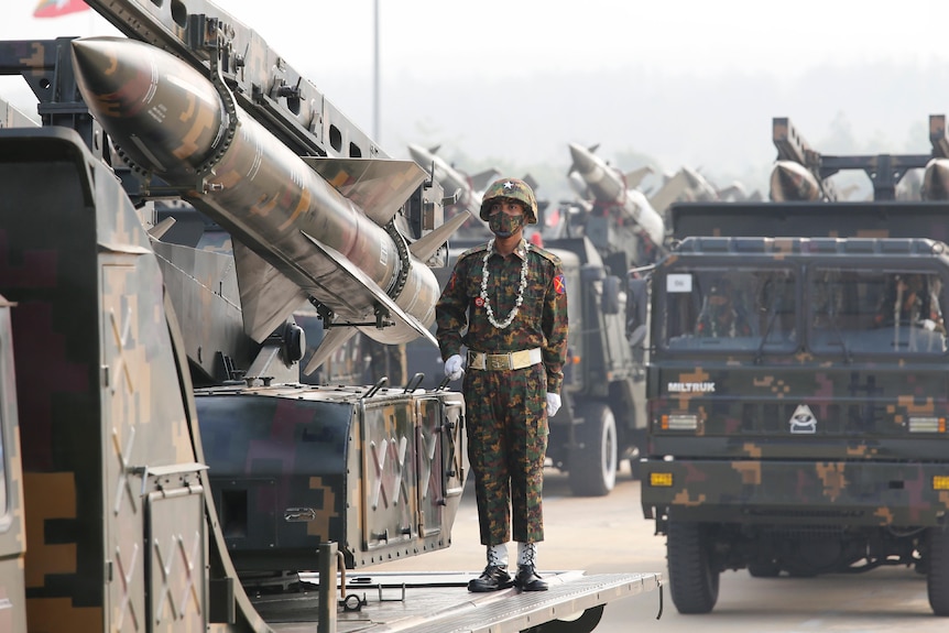 Military personnel participate in a parade alongside tanks with missiles.