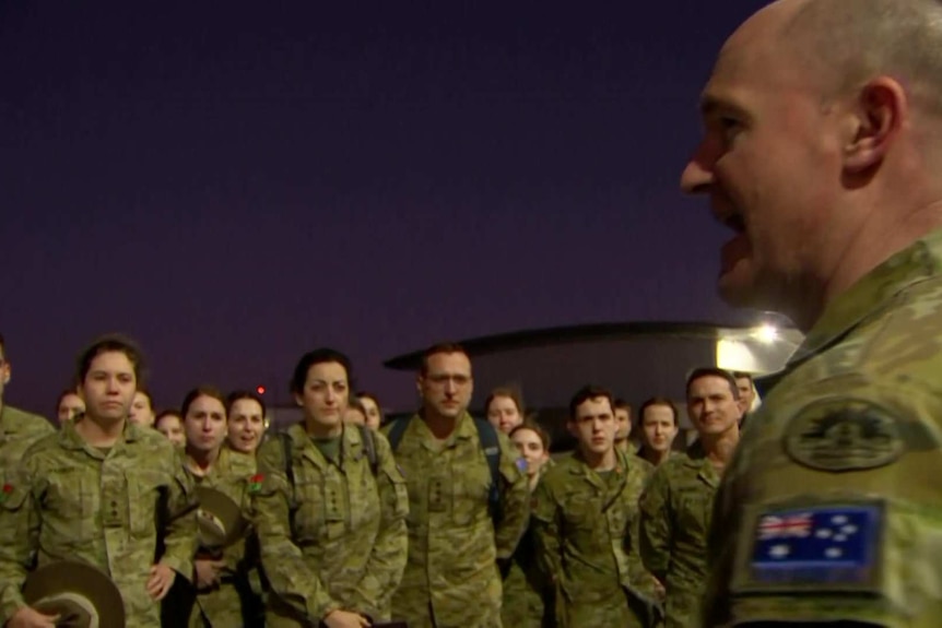 Australian Defence Force personnel wearing camouflaged uniforms get a briefing at the airport.