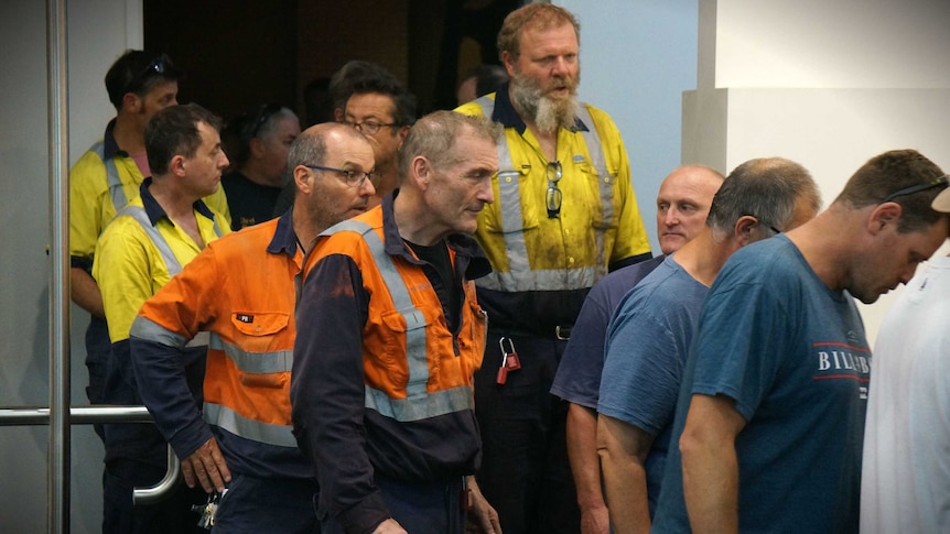 Steel workers in hi-vis shirts file out of a mass meeting.