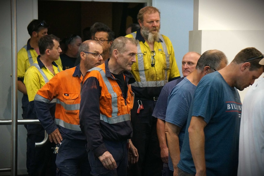 Steel workers in hi-vis shirts file out of a mass meeting.