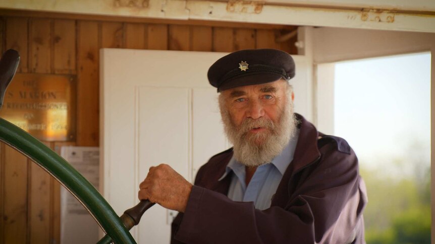 A paddlesteamer captain holds the wheel of the boat.