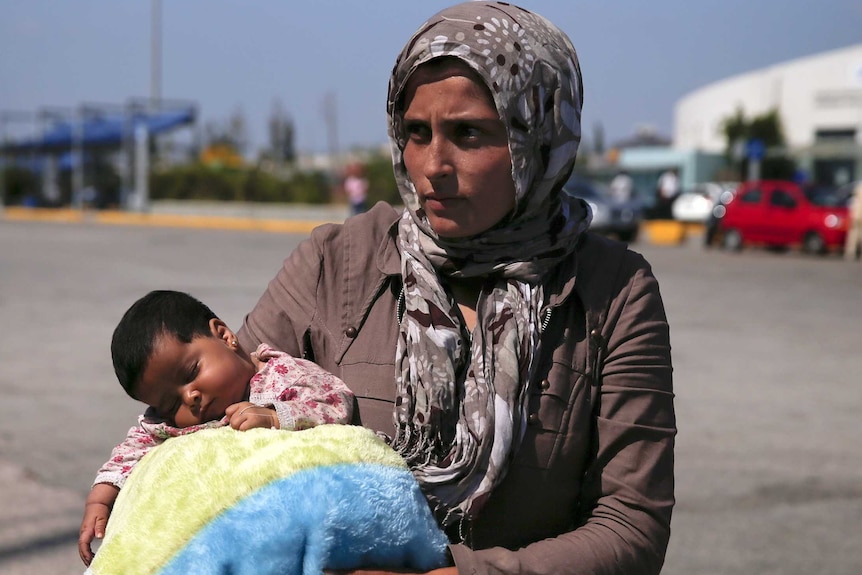 Syrian refugee holds her baby after their arrival at the port of Piraeus, near Athens