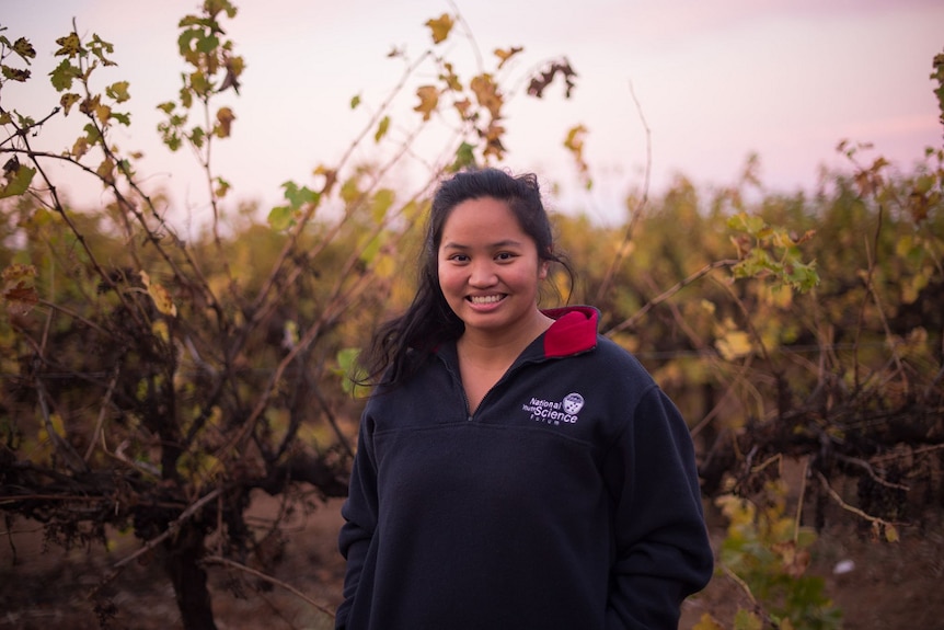 A woman is standing in the middle of vines, smiling.